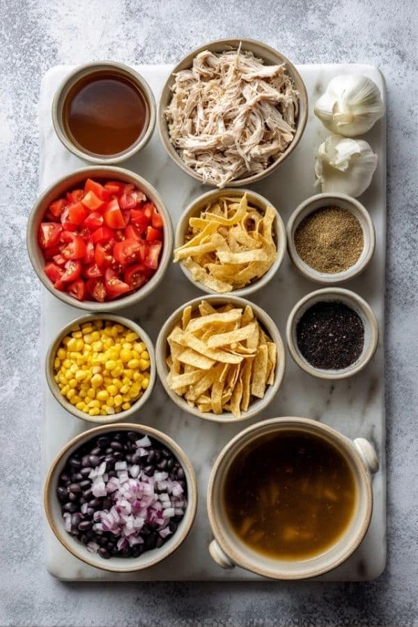 Ingredients for cozy Crockpot soup recipes including chicken, onions, carrots, celery, beans, tomatoes, and broth arranged on a rustic board